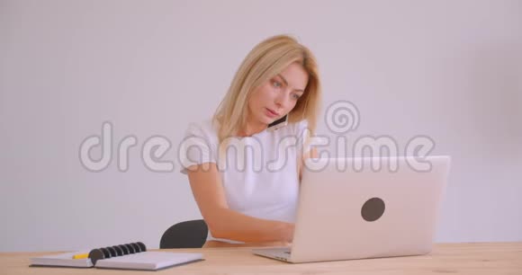 使用笔记本电脑在办公室内打电话的白种人金发成年雇员的特写照片视频的预览图