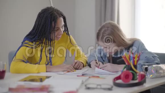 嘲笑坐在桌子旁做作业的朋友白人和非裔美国学生玩得开心青少年视频的预览图