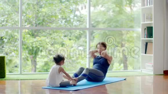 小女孩帮妈妈做健身垫上的运动视频的预览图