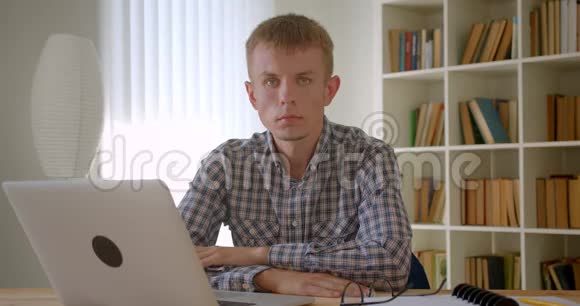 白种人商人在笔记本电脑前冷静地观看镜头集中在书架背景上视频的预览图