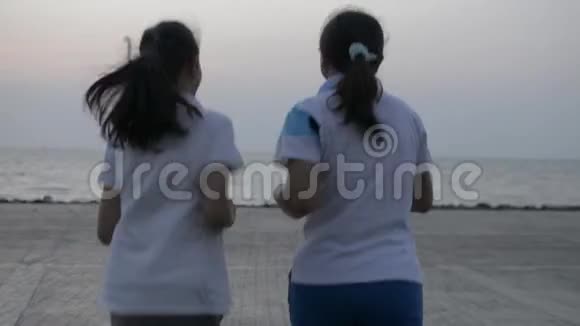 母亲和女儿一起慢跑到海岸的后景早上在普吉岛把手臂举到空中视频的预览图
