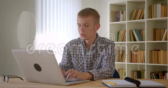 白种人商人专注地使用笔记本电脑和在书架背景上写笔记的肖像视频的预览图