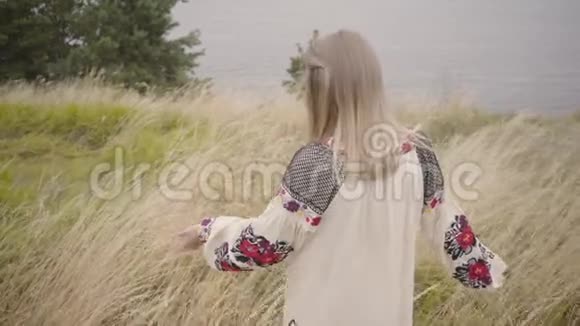 美丽的金发女孩穿着美丽的白色夏装刺绣走在高高的草地上这就是视频的预览图