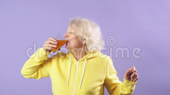 穿黄色运动衫的开朗的老太太喜欢新鲜胡萝卜汁视频的预览图