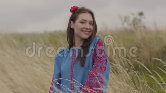 漂亮的年轻黑发女孩一头红花美丽的蓝色长夏装站在田野里视频的预览图