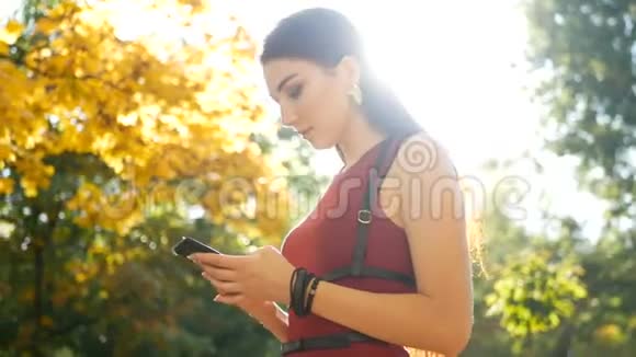 女性手持智能手机与绿色屏幕女孩在秋天公园散步时使用手机背面视频的预览图
