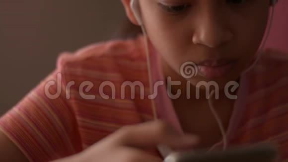 亚洲小女孩在家里看网上媒体时用手机带耳机视频的预览图