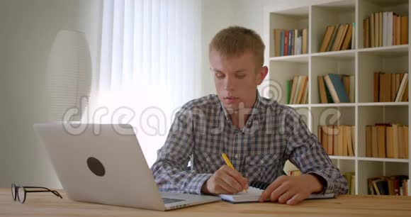 白种人商人专心地在笔记本电脑上打字和在书架背景上做笔记的肖像视频的预览图