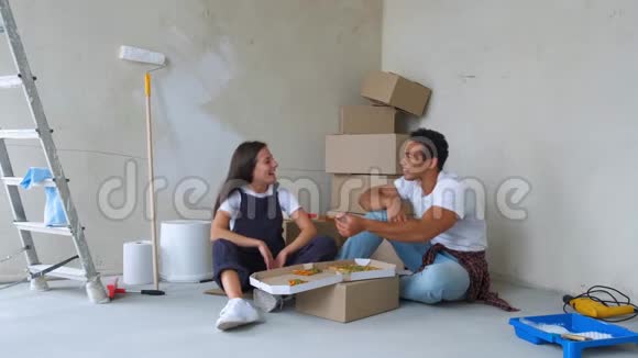 俯视着年轻夫妇在新公寓里坐在地板上吃披萨视频的预览图