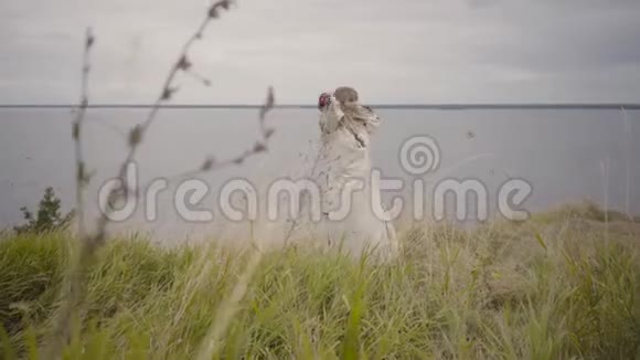 迷人的金发女孩穿着美丽的白色长夏礼服刺绣跳舞在草地上旋转这就是视频的预览图