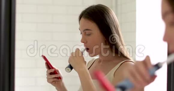 智能手机刷牙的年轻女子视频的预览图
