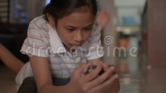 亚洲可爱的女孩躺在地板上在家里用手机社交女少年看视频视频的预览图
