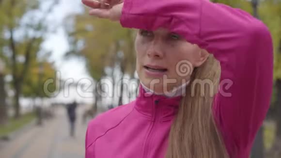 一位穿着粉红色运动服的疲惫的白种人女运动员的特写肖像她喝着水擦着额头自信视频的预览图