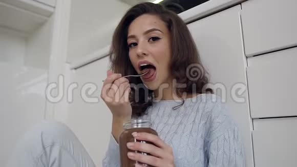 穿上时髦衣服的美丽快乐的女士用勺子在厨房里品尝美味的巧克力奶油视频的预览图