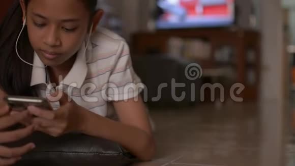 亚洲可爱的女孩躺在地板上在家里用手机社交女少年看音乐视频视频的预览图