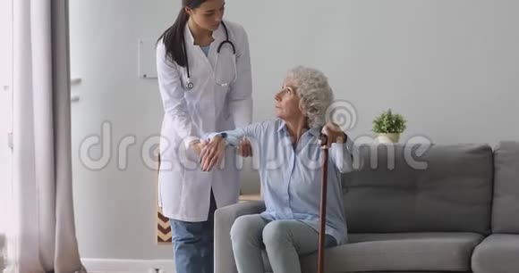 年轻女性护理员帮助年长祖母手持拐杖视频的预览图