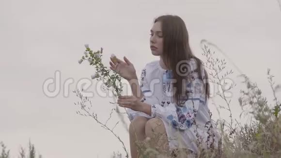 漂亮的年轻黑发女孩穿着长长的刺绣连衣裙手里拿着野花那个女孩摸着紫罗兰视频的预览图