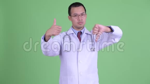 困惑的亚洲男子医生戴着眼镜在拇指向上和拇指向下之间选择视频的预览图