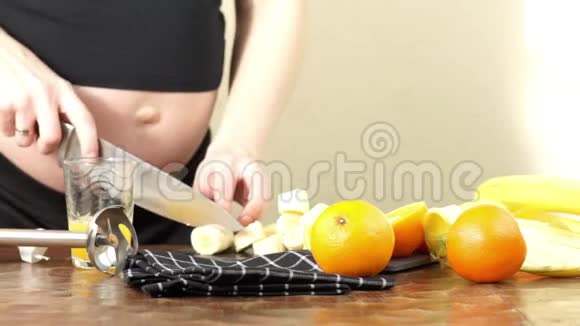 孕妇在厨房里做健康的冰沙香蕉和橘子切片视频的预览图