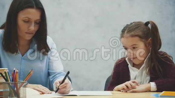在灰色背景下把妈妈和女儿关起来在这期间她为一个微笑的女儿写作业概念视频的预览图