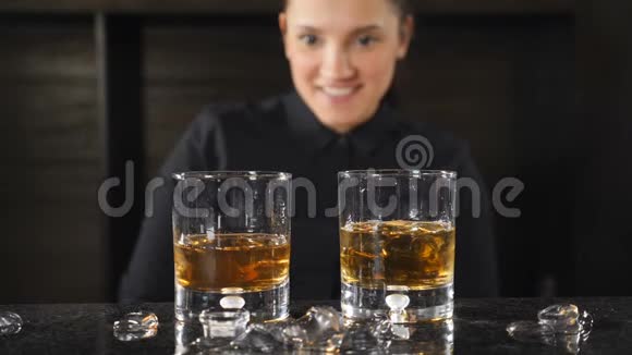 微笑着的女酒保透过站在柜台后面的威士忌酒杯看镜头的肖像视频的预览图
