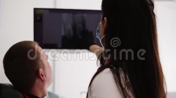 白人女性牙医向男性患者解释屏幕上的x射线图像显示了不健康牙齿的形象视频的预览图
