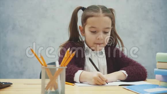 一个漂亮的女学生在灰色背景下坐在桌子旁在此期间他进行练习和写作视频的预览图