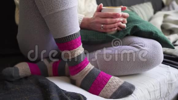 粉色和棕色温暖的羊毛袜特写一个女人坐在沙发上带着一杯白色的热饮上面有一个格子呢视频的预览图