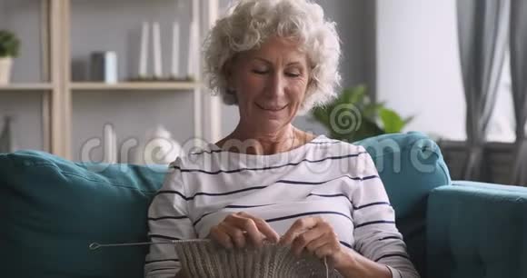年长的成熟女人在家里的沙发上轻松编织视频的预览图