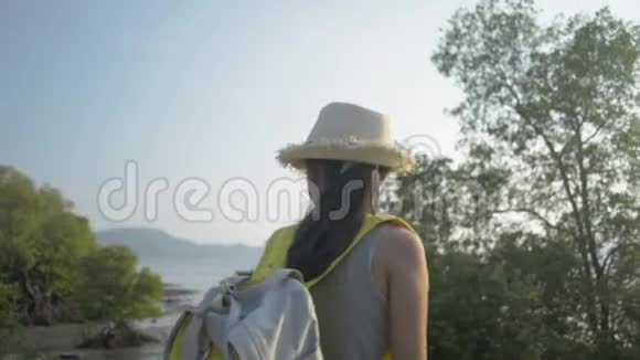 可爱的亚洲女孩戴着带背包的草帽欣赏日落时带着红树林的海岸美景视频的预览图