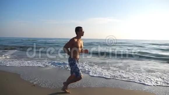 运动帅哥在海岸慢跑与美丽的海景背景年轻的运动员沿着海洋奔跑视频的预览图