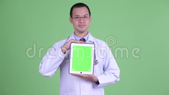 快乐的亚洲男子医生一边思考一边展示数码平板电脑视频的预览图