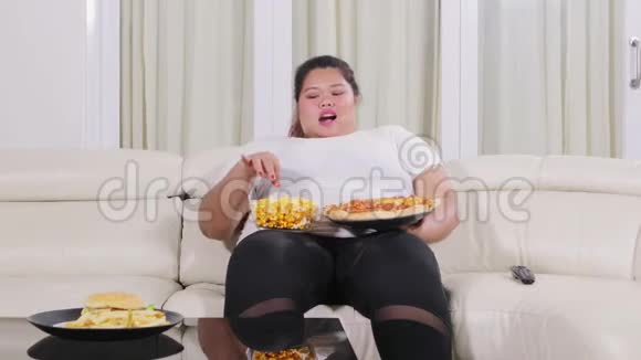 超重妇女在沙发上吃垃圾食品视频的预览图