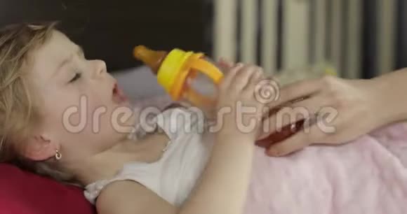 可爱的女婴睡在家里舒适的床上喝着瓶子里的果汁视频的预览图