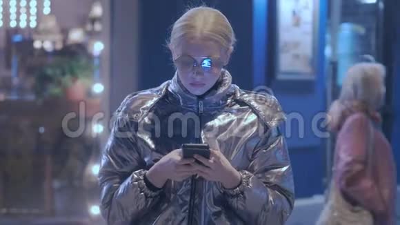 一个年轻的少女站在一条城市街道上拿着智能手机输入短信与朋友的通讯视频的预览图