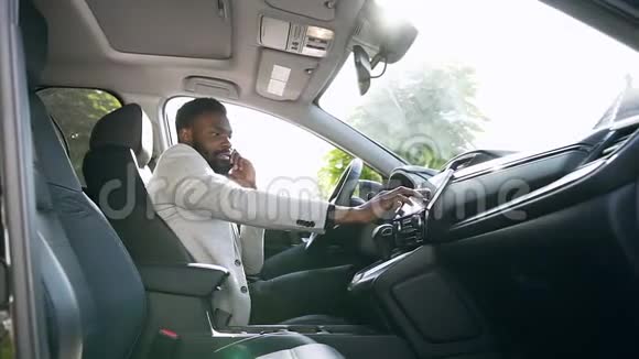 英俊的非洲裔美国年轻人坐在前皮座椅黑色豪华车上并调整车辆触摸视频的预览图