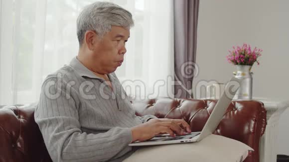 老人在客厅的笔记本电脑上打字聊天视频的预览图