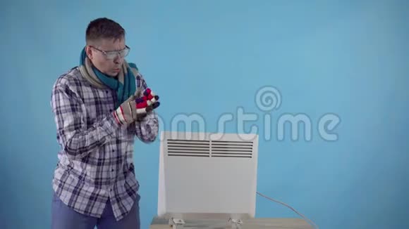 冰冻的男人身上覆盖着霜冻和手套在蓝色背景电加热器旁边加热视频的预览图