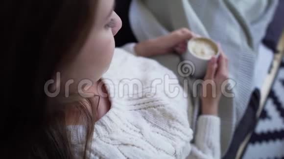 一位穿着白色针织毛衣的年轻女子双手捧着一边喝着咖啡一边拍着肩膀视频的预览图
