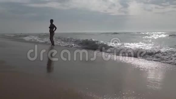 一位剪影中的女士欣赏着海滩上海水中的一个美丽而美丽的日出视频的预览图
