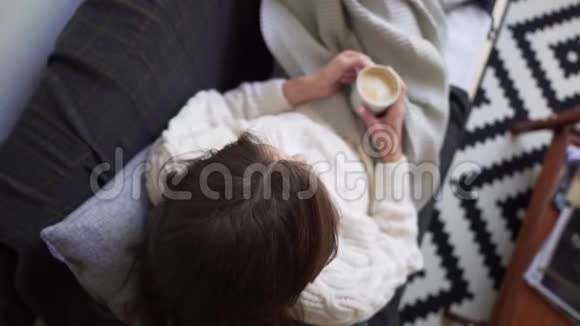 俯视图一个女孩喝热咖啡躲在毯子里躺在沙发上Hygge概念视频的预览图