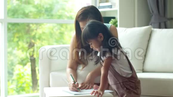 年轻的母亲一边教女儿一边画纸视频的预览图