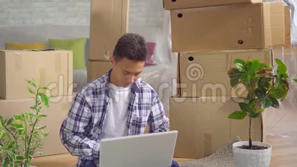 年轻有思想的亚洲人搬到一间新公寓后坐在地上的笔记本电脑旁视频的预览图