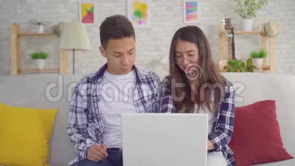 年轻积极的亚洲夫妇坐在笔记本电脑的客厅里视频的预览图