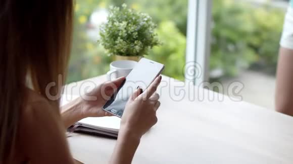 坐在玻璃窗户附近的年轻女子使用智能手机付款视频的预览图