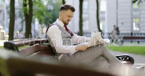 一个穿西装留胡子的富人坐在公园里看报纸视频的预览图