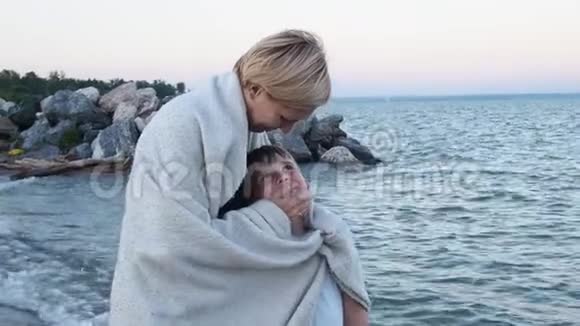 妈妈在海滩上拥抱她的儿子把他的毯子包起来这样会暖和他用手抚摸男孩的脸他们微笑着视频的预览图