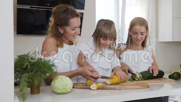 年轻的母亲教孩子们如何在家厨房里切蔬菜这位年轻女子和她的两个女儿正在切视频的预览图