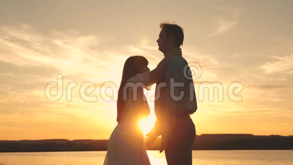 年轻夫妇在海滩上日落时旋转和跳舞爱的男人和女人在湖的背景下跳舞视频的预览图