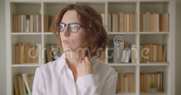 戴眼镜的白种人成年女商人的特写肖像在室内展望书架上放着书架视频的预览图